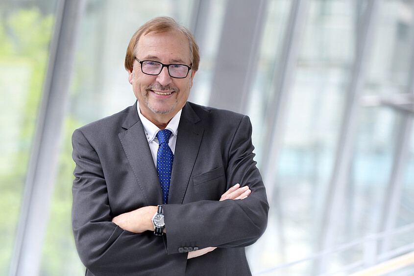 Prof. Dr. med. Siegfried Jedamzik steht mit verschränkten Armen lächelnd vor einer Glasfassade.